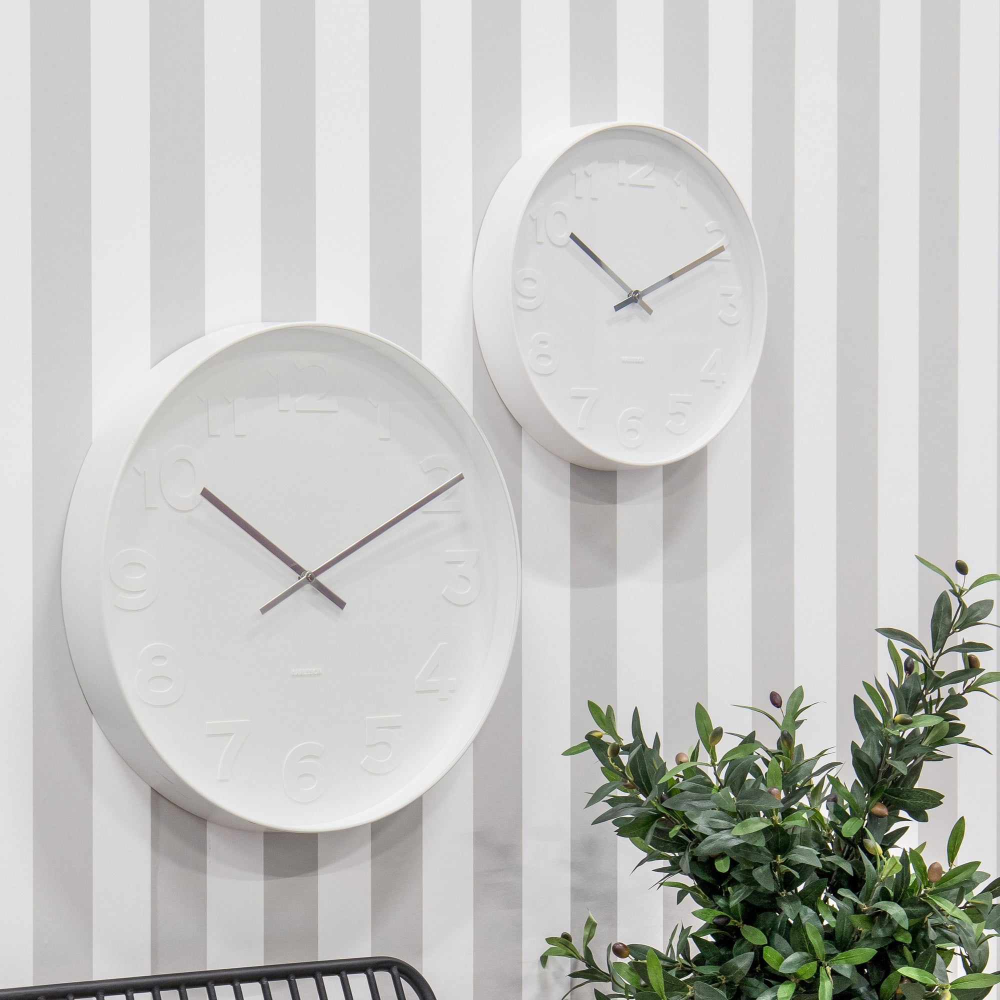 Two white wall clocks hung on grey and white stripe wall